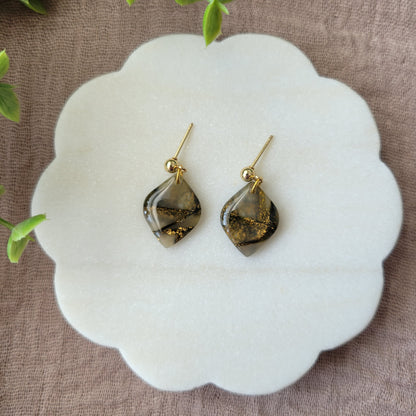 Top view of a pair of moss green marble diamond shaped earrings displayed on a white round scalloped tray.