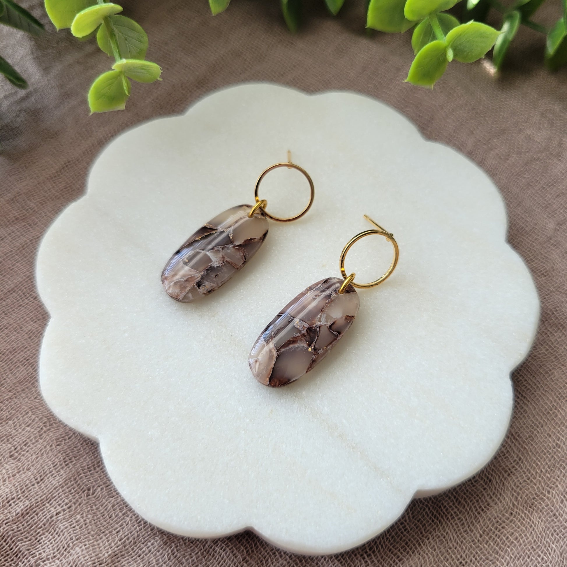 Right side view of a pair of brown marble long oval earrings displayed on a white round scalloped tray.