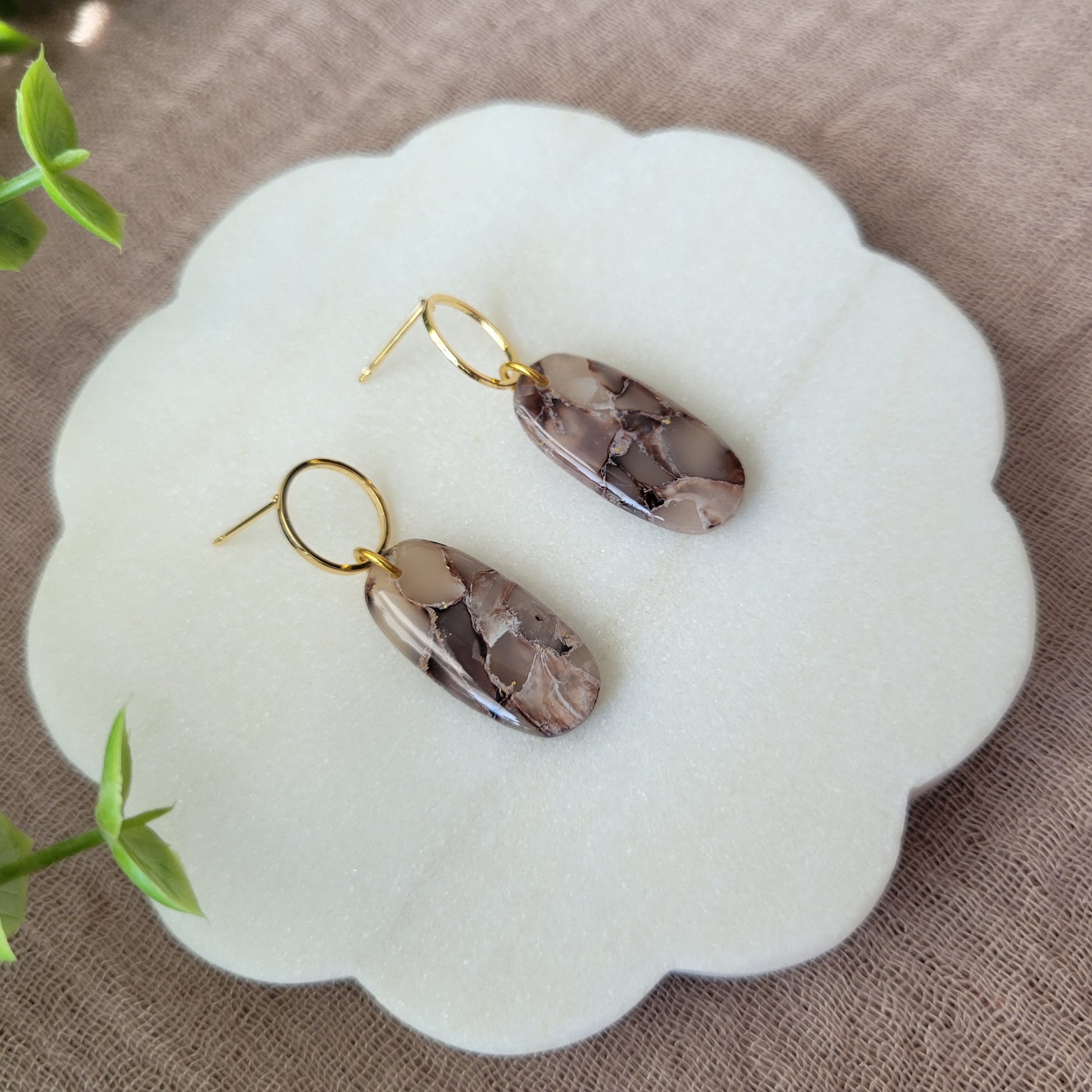 Left side view of a pair of brown marble long oval earrings displayed on a white round scalloped tray.