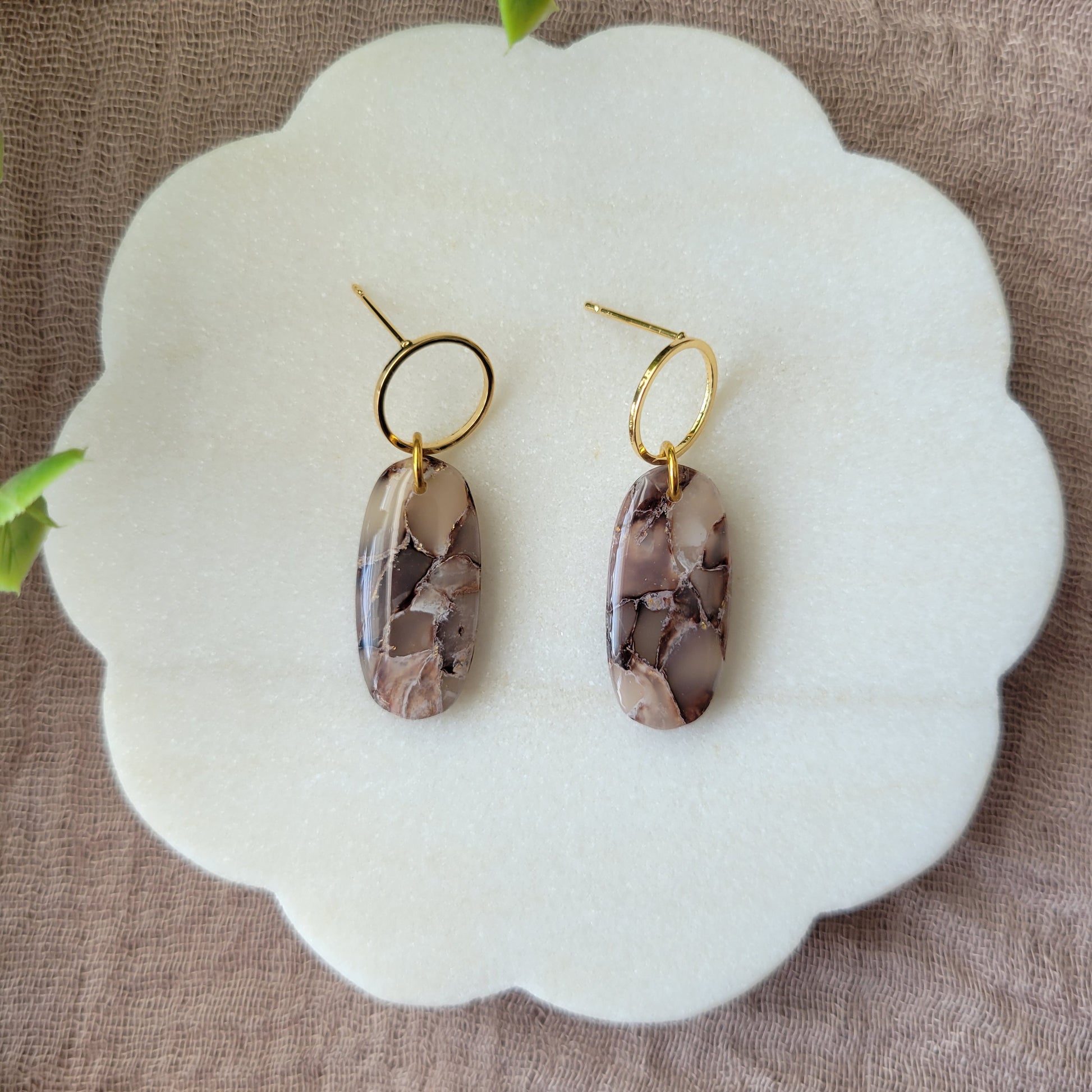 Top view of a pair of brown marble long oval earrings displayed on a white round scalloped tray.