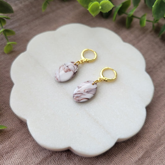 Right side view of a pair of brown, white marble oval shaped earrings displayed on a white round scalloped tray.