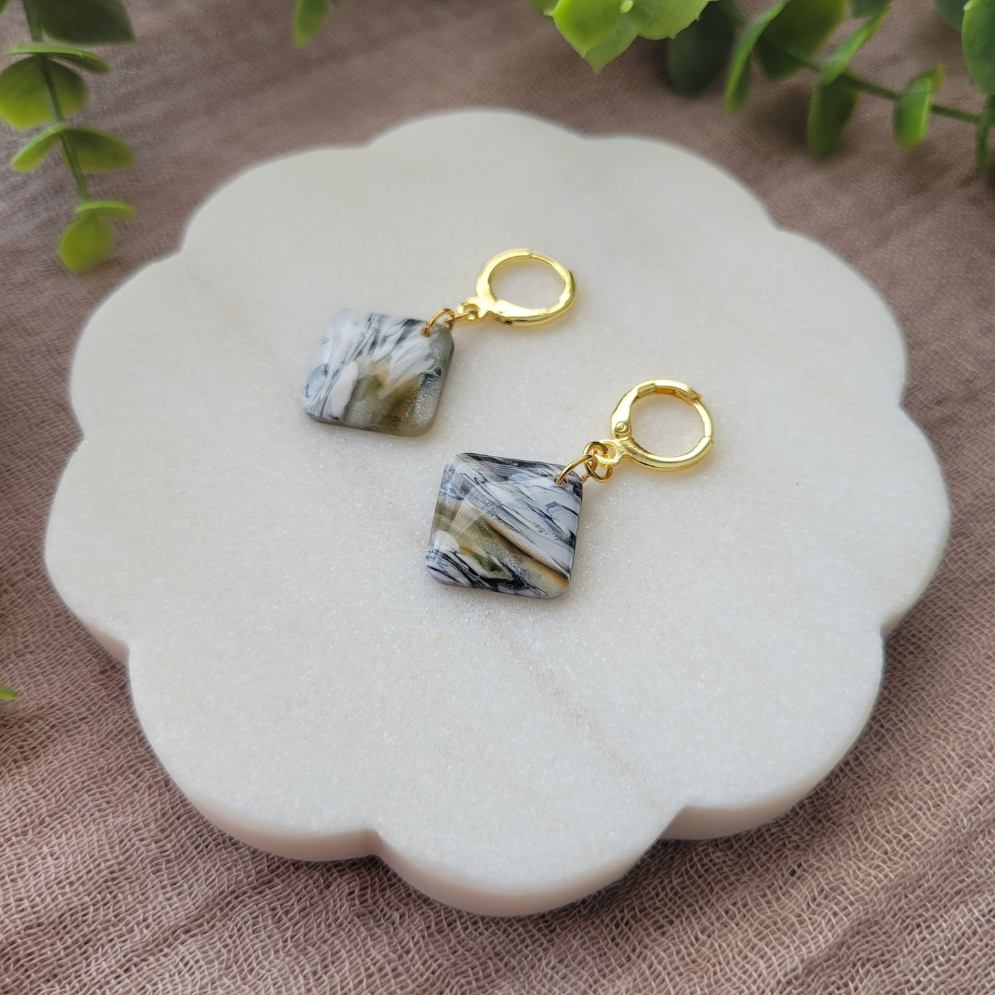 Right side view of a pair of black, white, brown, moss square shaped earrings displayed on a white round scalloped tray.