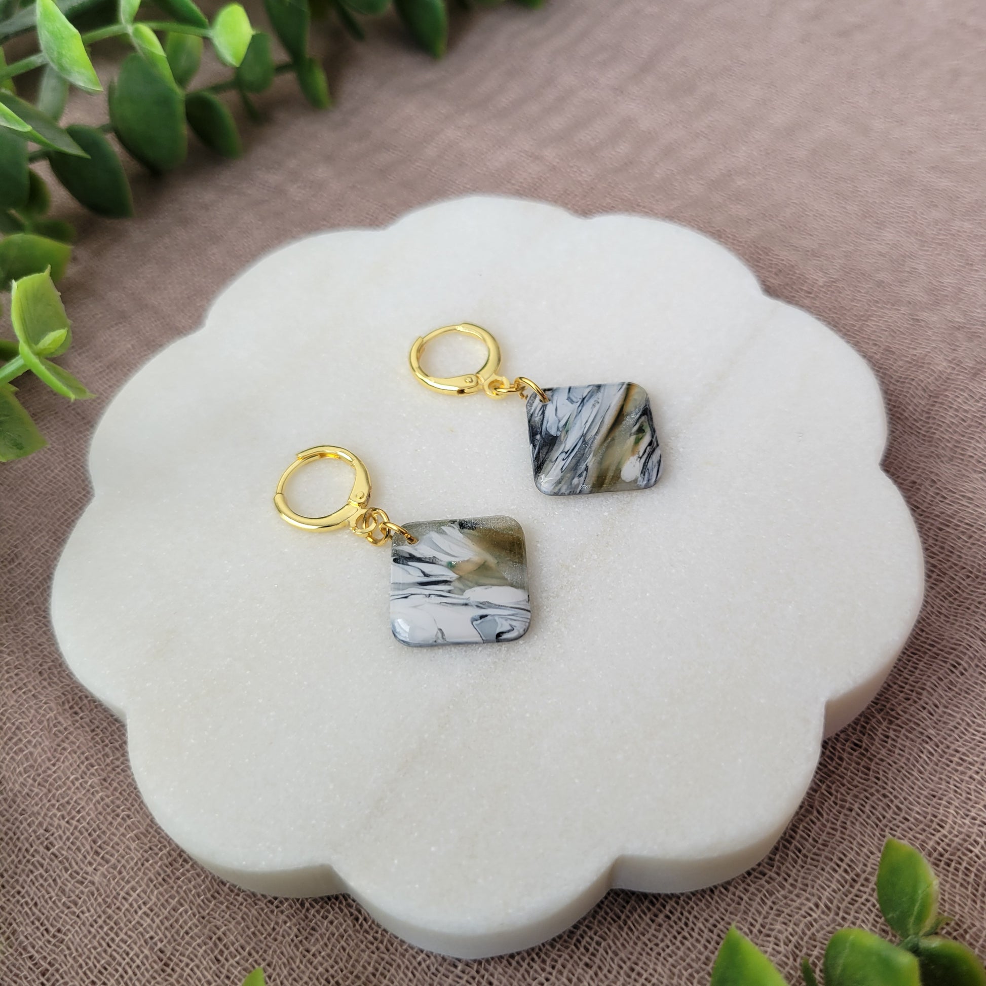 Left side view of a pair of black, white, brown, moss square shaped earrings displayed on a white round scalloped tray.