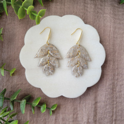 Top view of a pair of gold, white flower shaped earrings displayed on a white round scalloped tray.