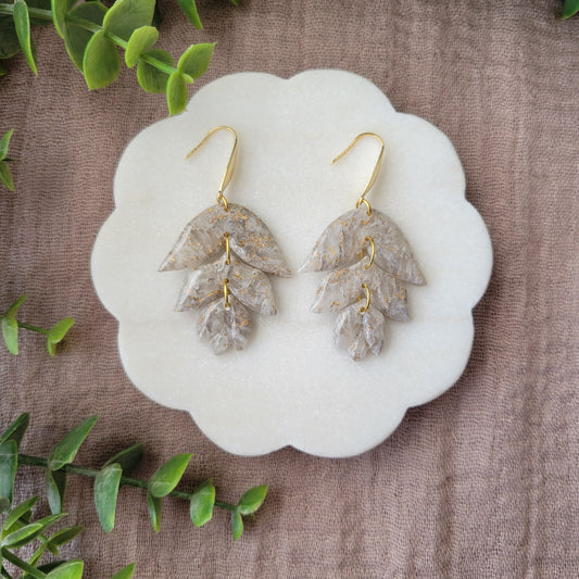 Top view of a pair of gold, white flower shaped earrings displayed on a white round scalloped tray.