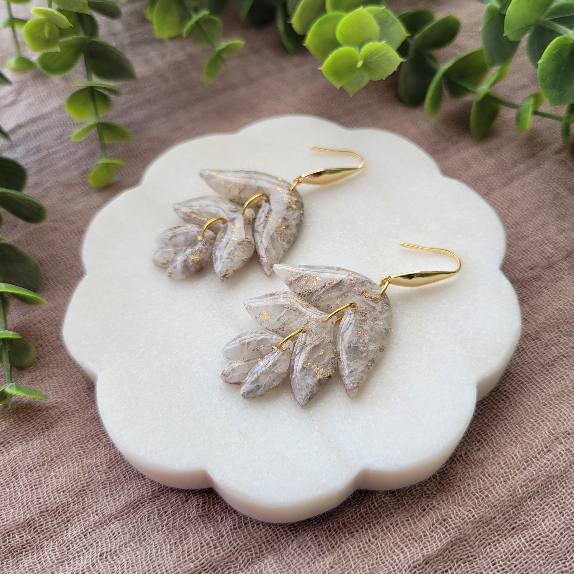 Right side view of a pair of gold, white flower shaped earrings displayed on a white round scalloped tray.