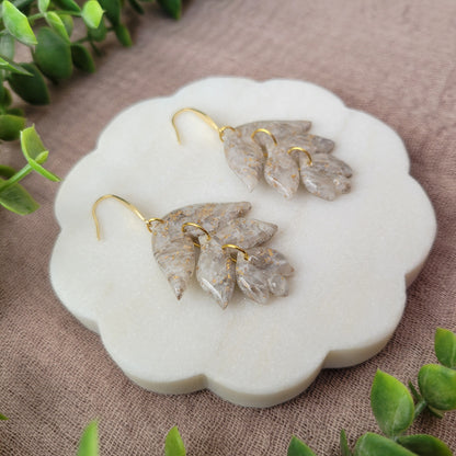 Left side view of a pair of gold, white flower shaped earrings displayed on a white round scalloped tray.