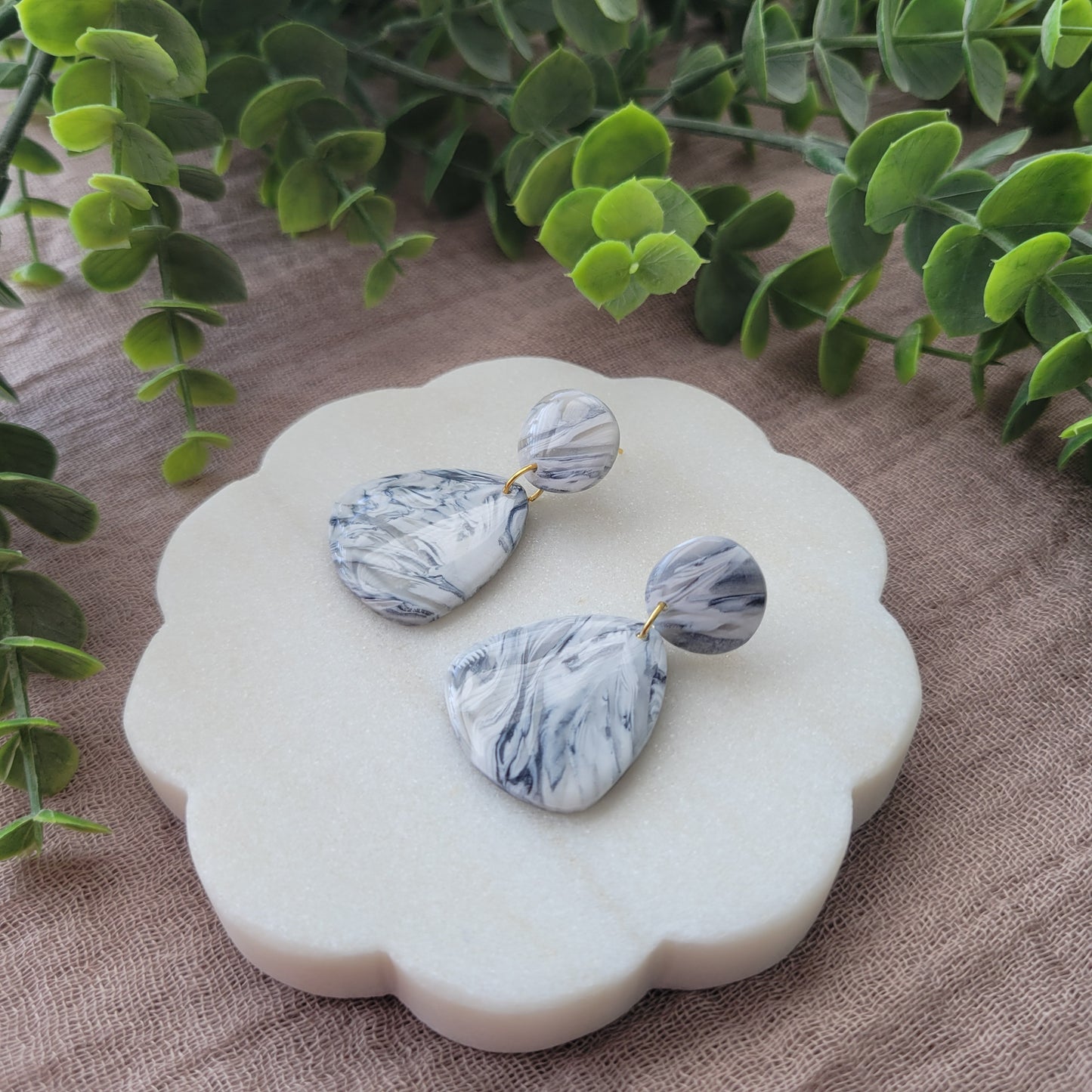 Right side view of a pair of black, white marble organic shaped earrings displayed on a white round scalloped tray.