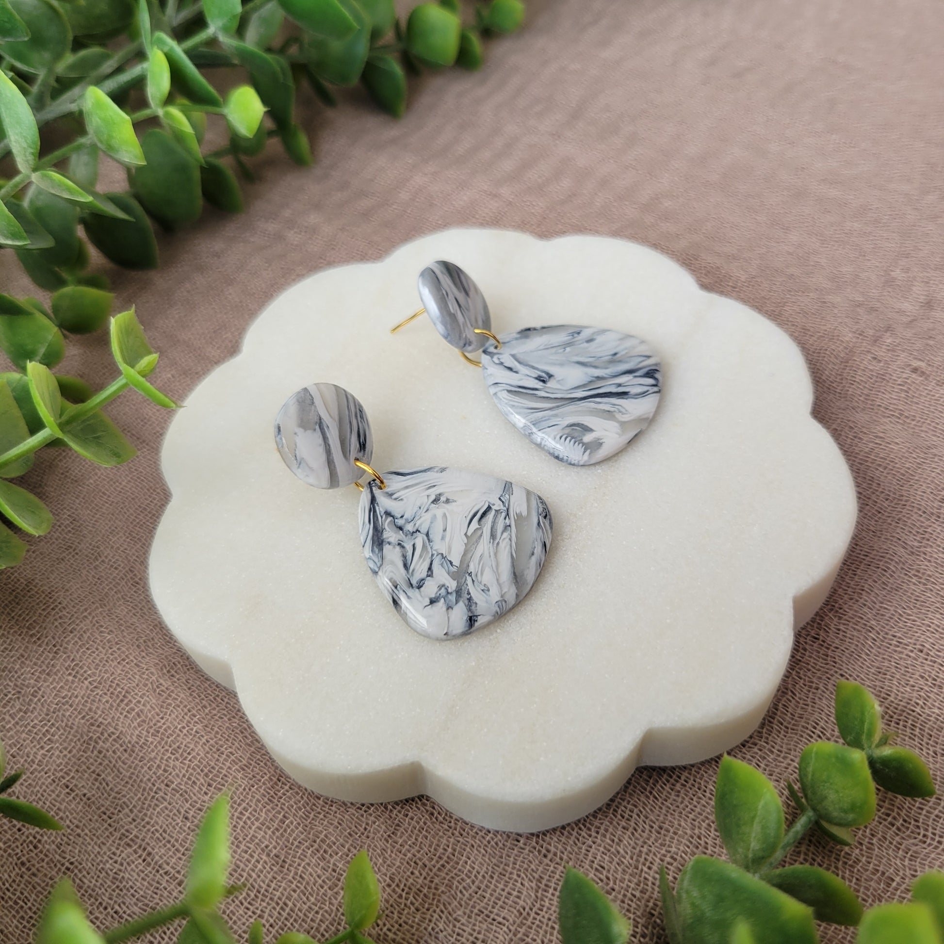 Left side view of a pair of black, white marble organic shaped earrings displayed on a white round scalloped tray.