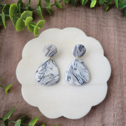 Top view of a pair of black, white marble organic shaped earrings displayed on a white round scalloped tray.