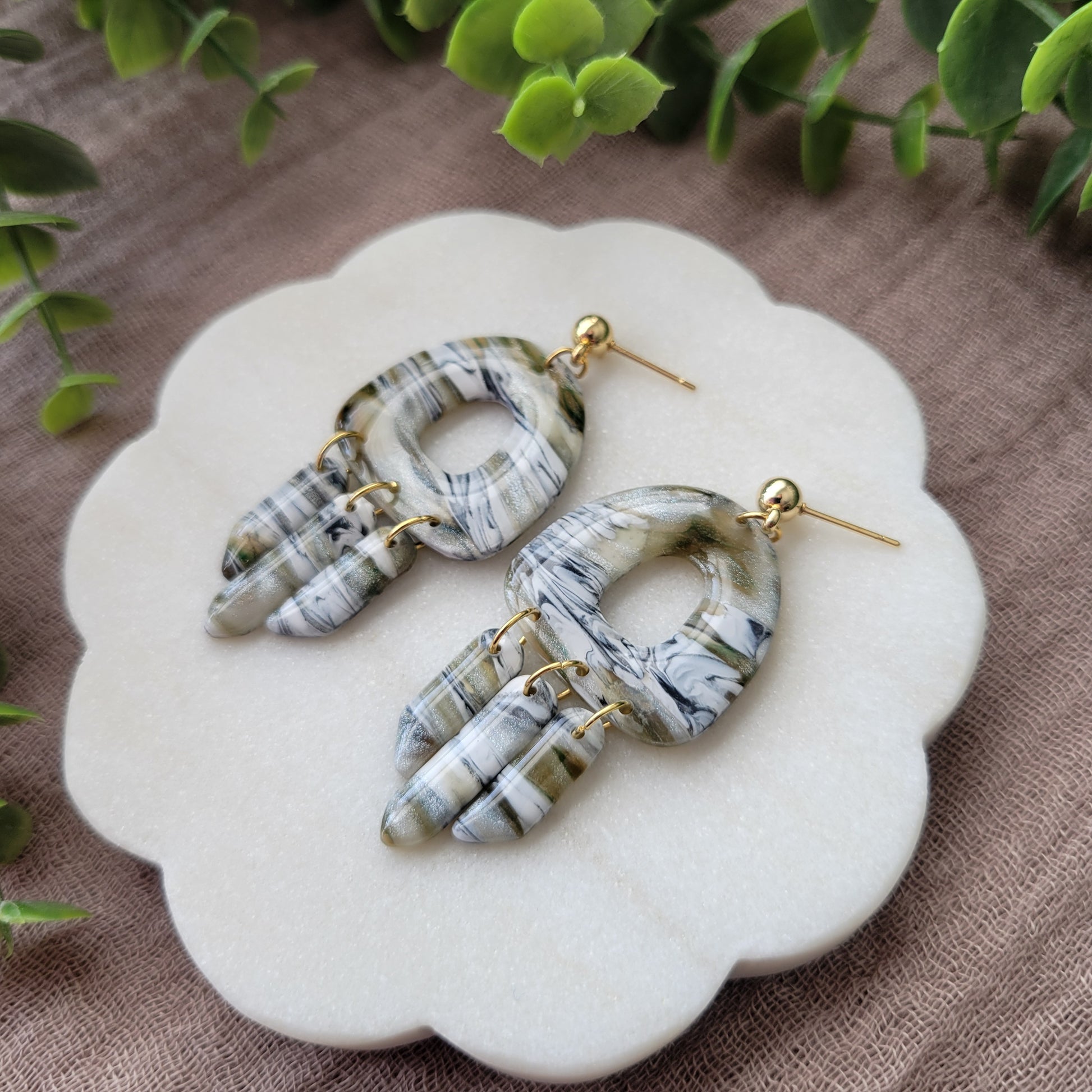 Right side view of a pair of green, white, black, brown marbled earrings displayed on a white round scalloped tray.