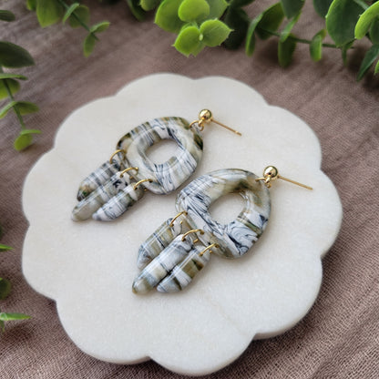 Right side view of a pair of green, white, black, brown marbled earrings displayed on a white round scalloped tray.
