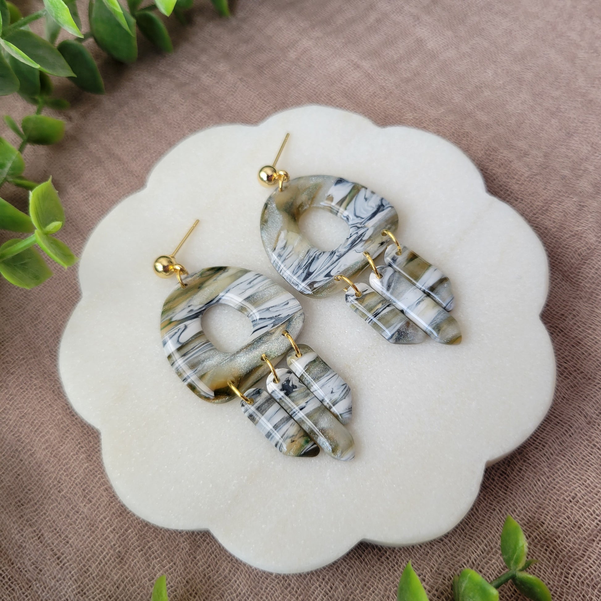 Left side view of a pair of green, white, black, brown marbled earrings displayed on a white round scalloped tray.