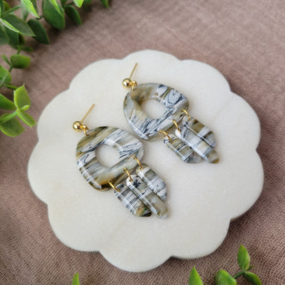 Left side view of a pair of green, white, black, brown marbled earrings displayed on a white round scalloped tray.