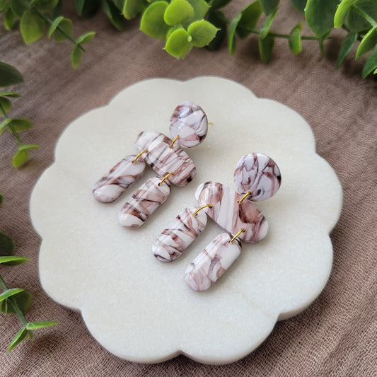 Right side view of a pair of brown, white marble stone shaped earrings displayed on a white round scalloped tray.