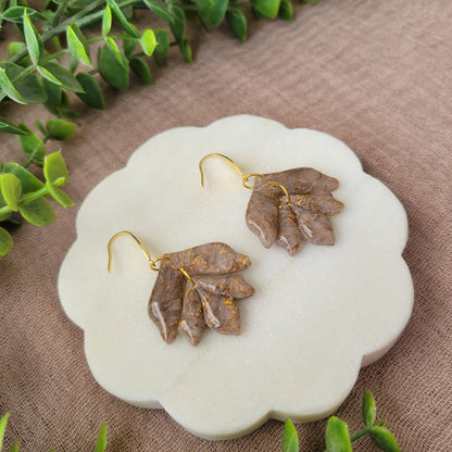 Left side view of a pair of white, bronze flower shaped earrings displayed on a white round scalloped tray.