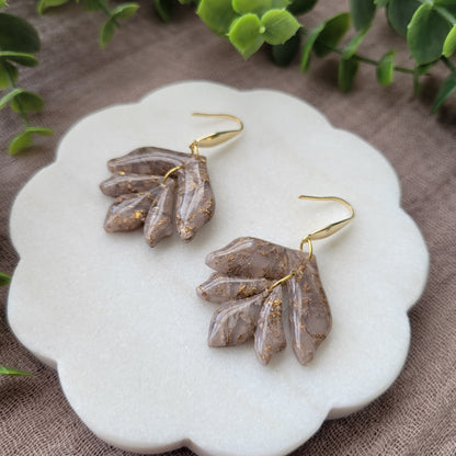 Right side view of a pair of white, bronze flower shaped earrings displayed on a white round scalloped tray.
