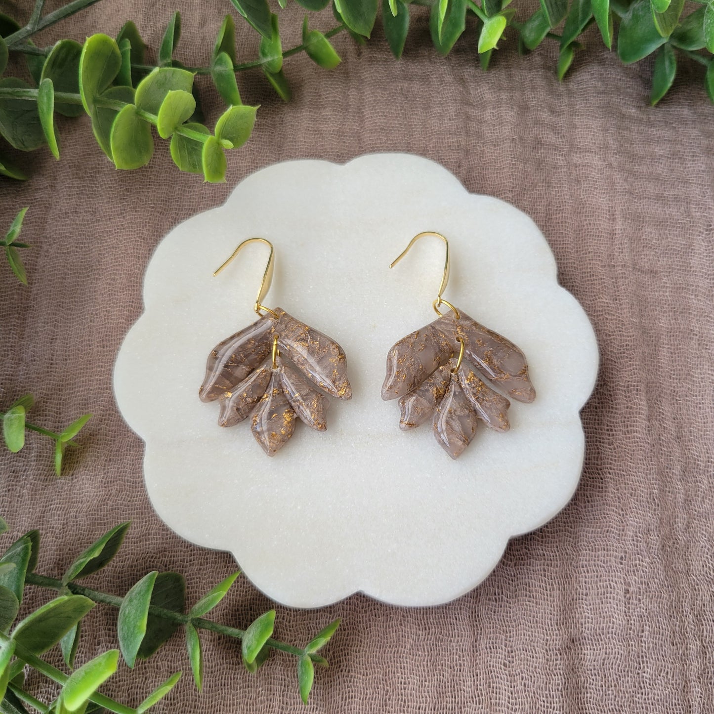 Top view of a pair of white, bronze flower shaped earrings displayed on a white round scalloped tray.