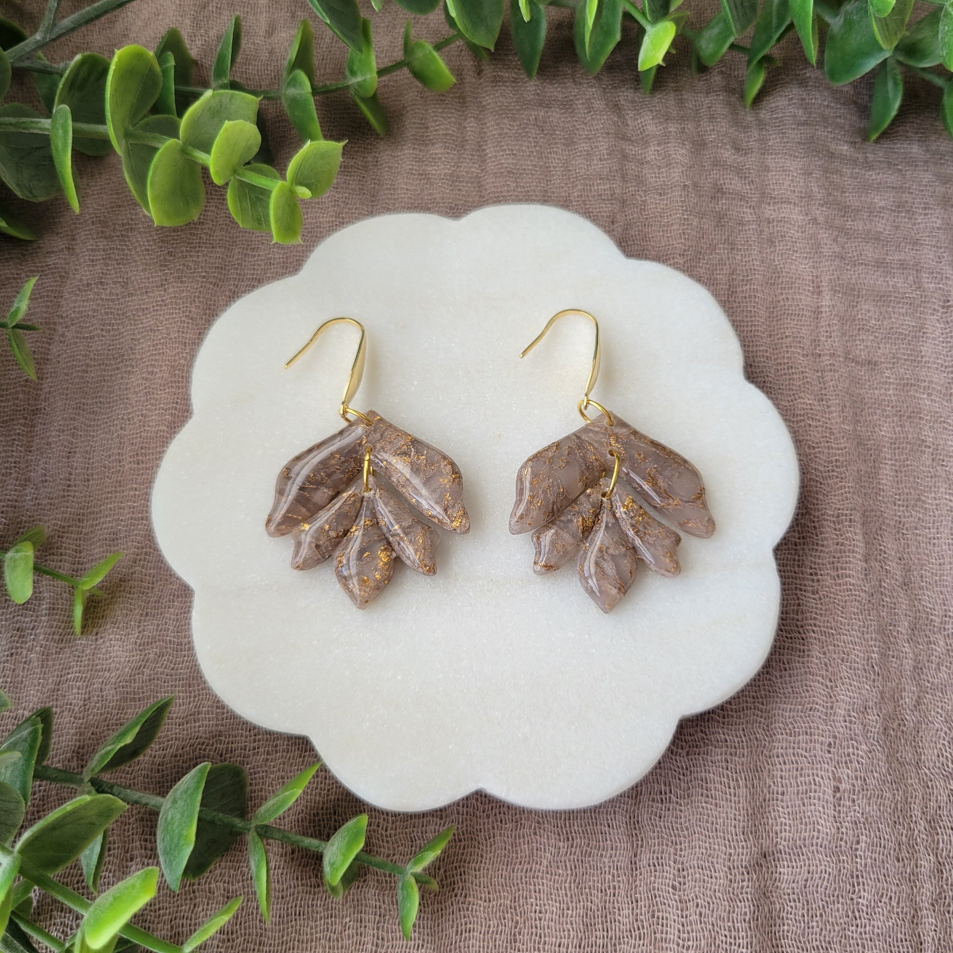 Top view of a pair of white, bronze flower shaped earrings displayed on a white round scalloped tray.