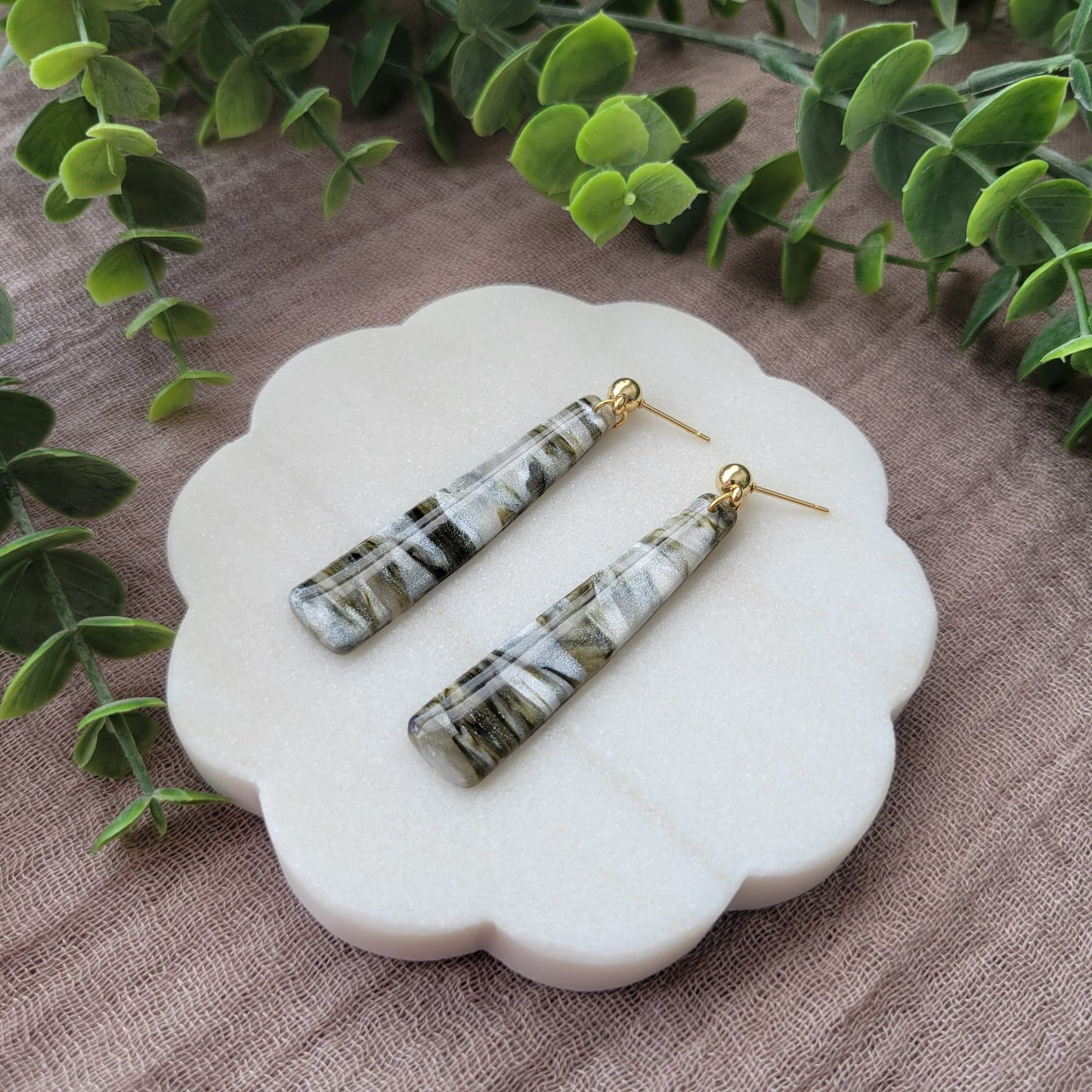 Right side view of a pair of moss, pearl colored pillar earrings displayed on a white round scalloped tray.
