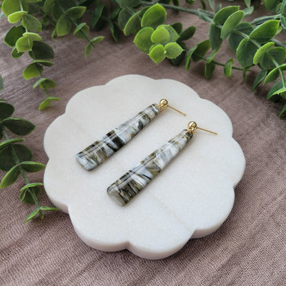 Right side view of a pair of moss, pearl colored pillar earrings displayed on a white round scalloped tray.