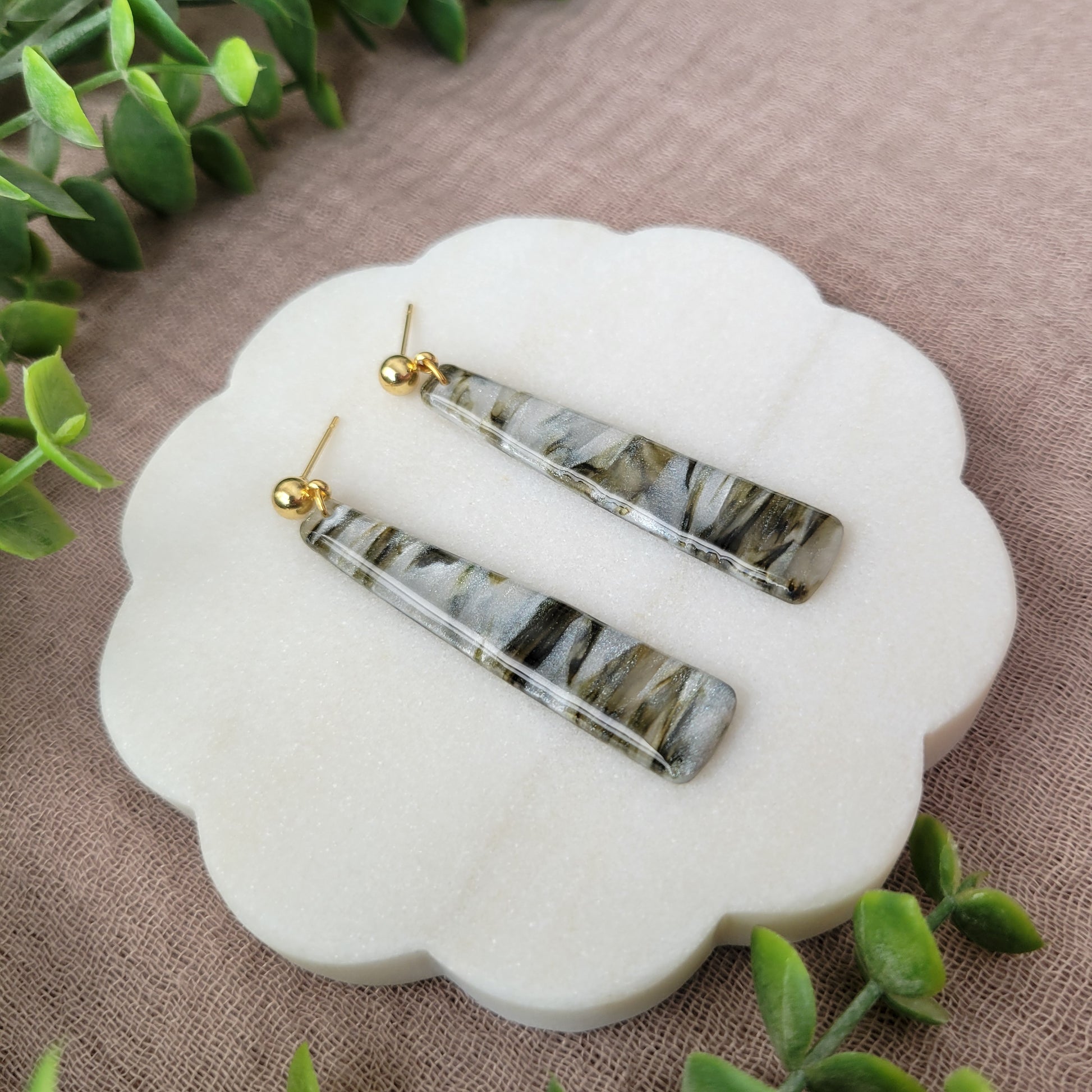 Left side view of a pair of moss, pearl colored pillar earrings displayed on a white round scalloped tray.