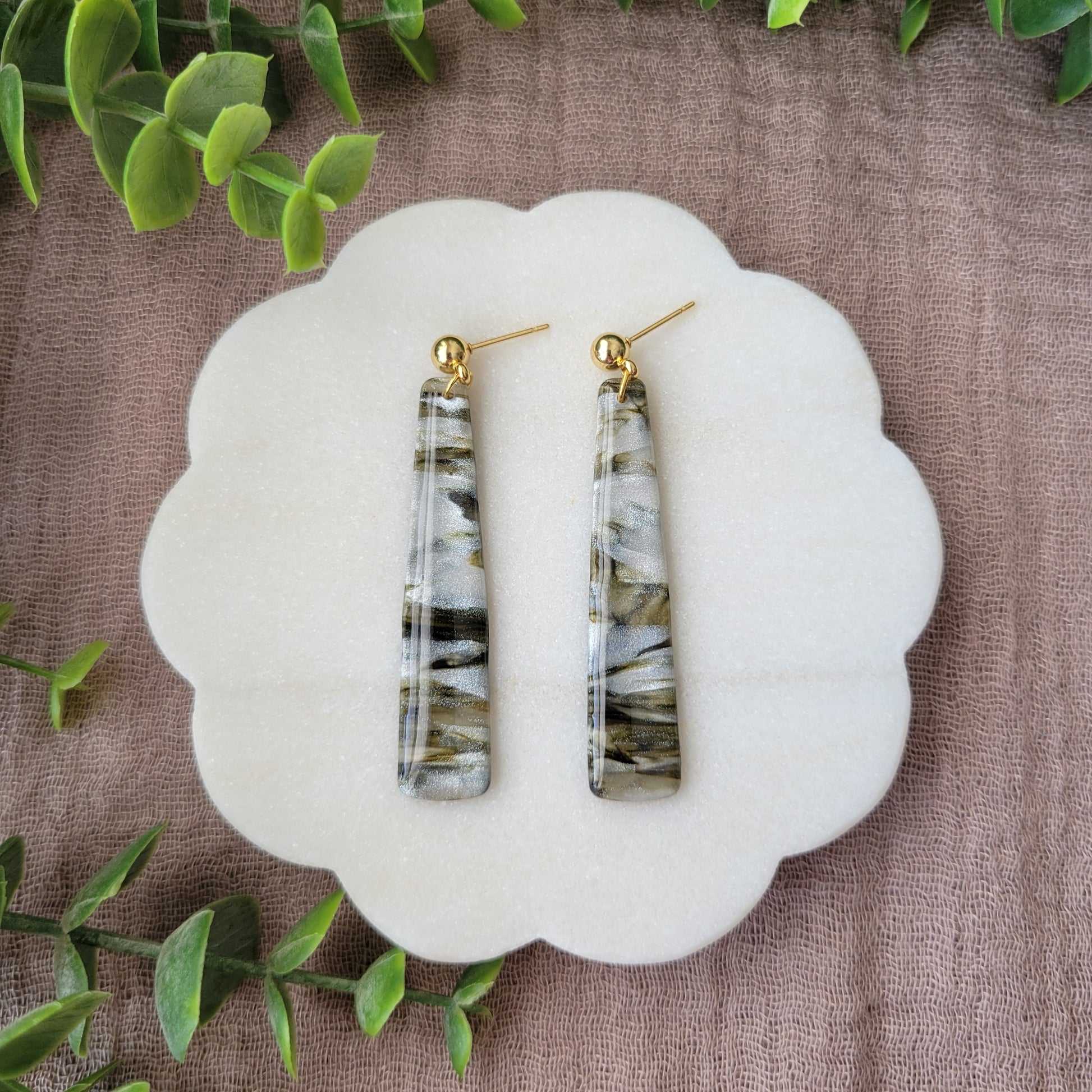 Top view of a pair of moss, pearl colored pillar earrings displayed on a white round scalloped tray.