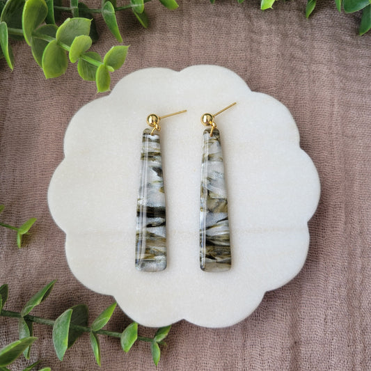 Top view of a pair of moss, pearl colored pillar earrings displayed on a white round scalloped tray.