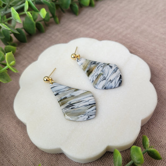 Left side view of a pair of black, white, brown, moss wide teardrop shaped earrings displayed on a white round scalloped tray.