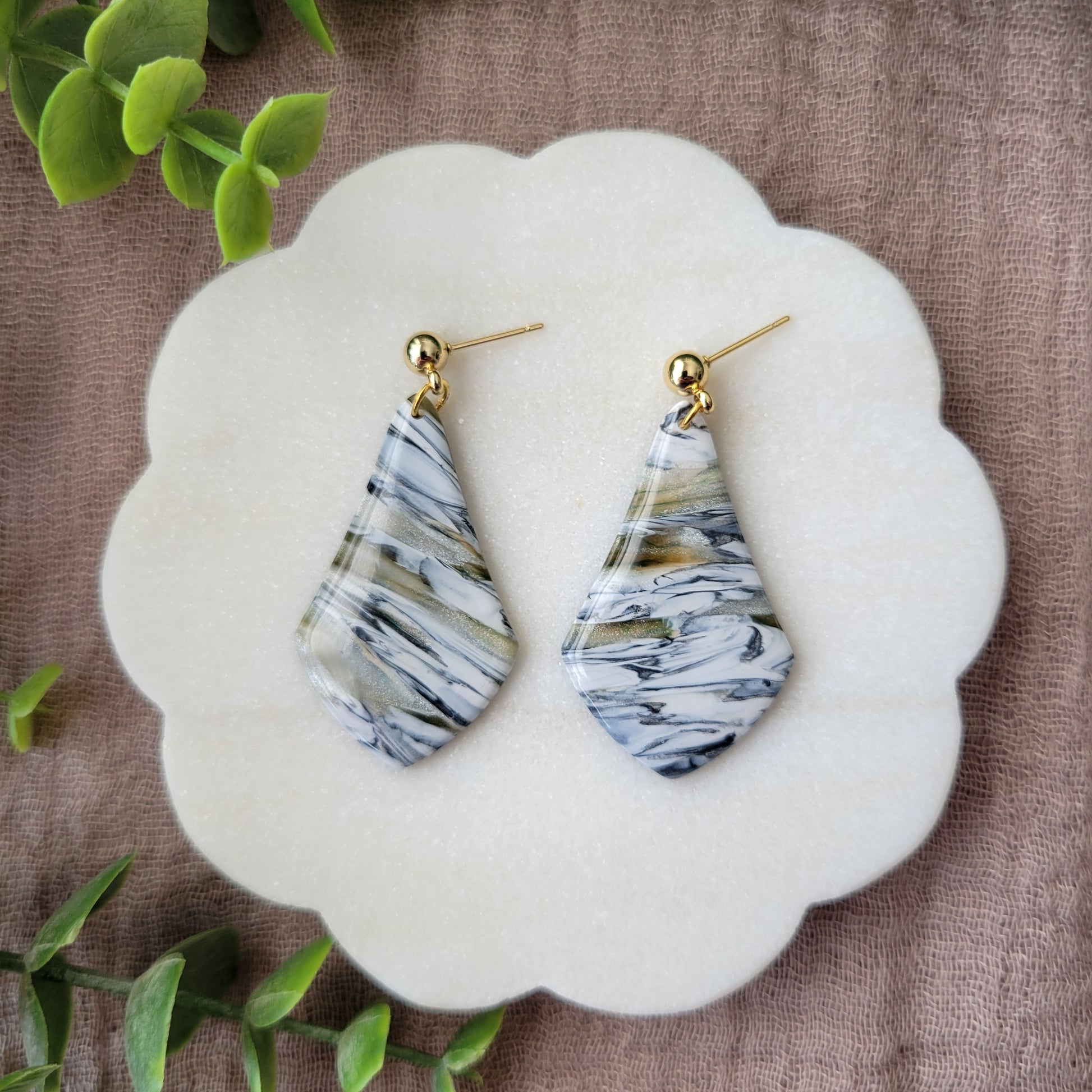 Top view of a pair of black, white, brown, moss wide teardrop shaped earrings displayed on a white round scalloped tray.