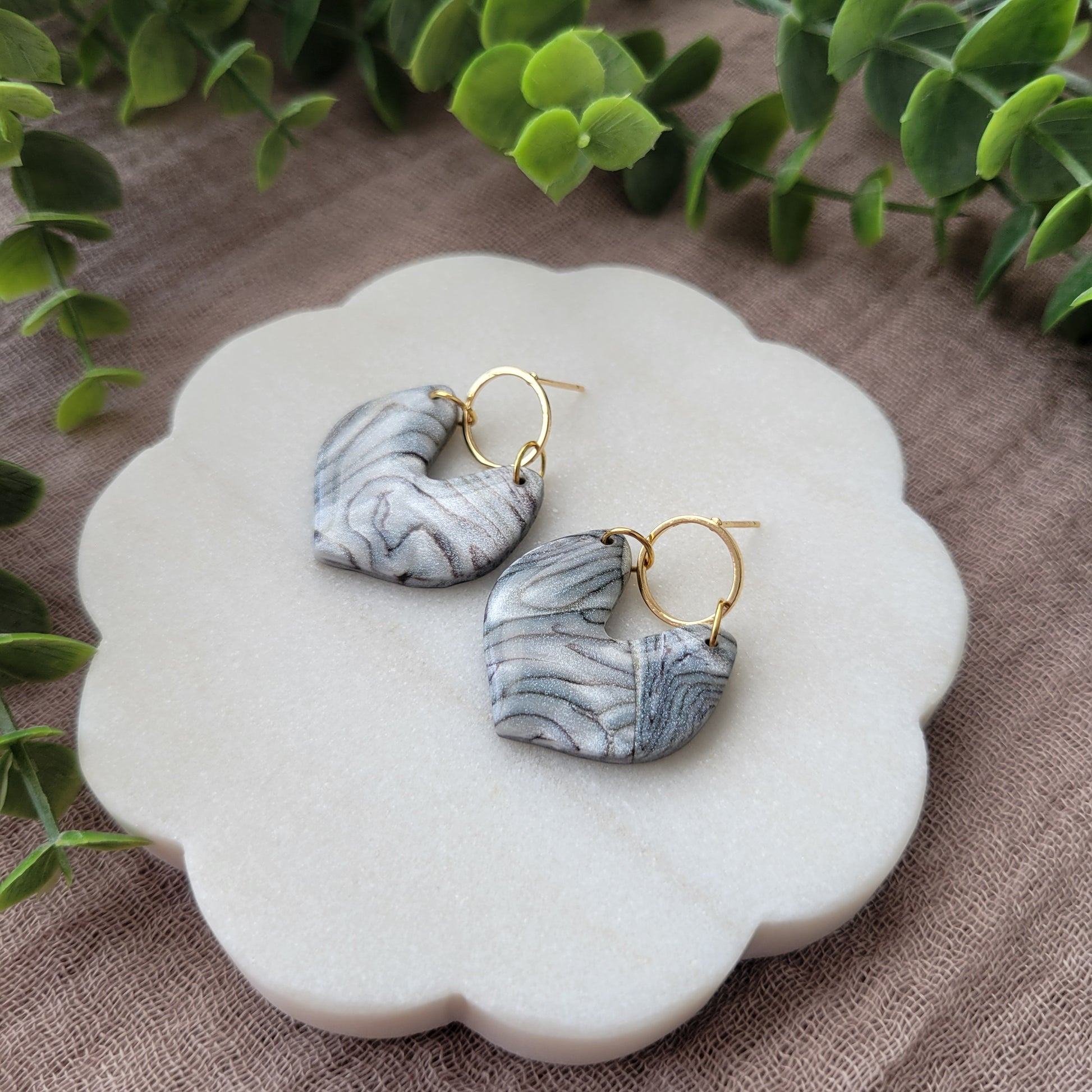Right side view of a pair of silver, brown earrings displayed on a white round scalloped tray.