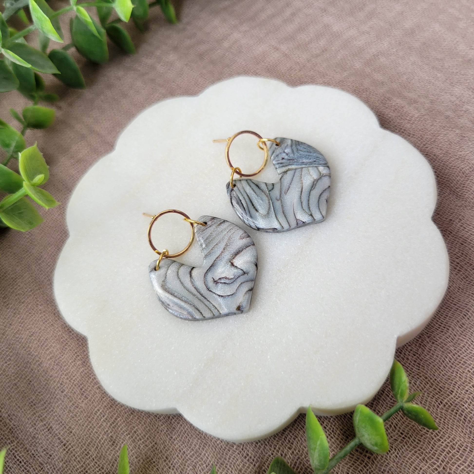 Left side view of a pair of silver, brown earrings displayed on a white round scalloped tray.