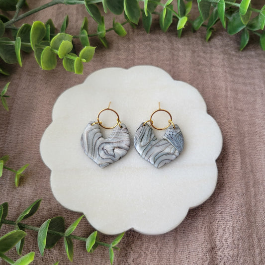 Top view of a pair of silver, brown earrings displayed on a white round scalloped tray.