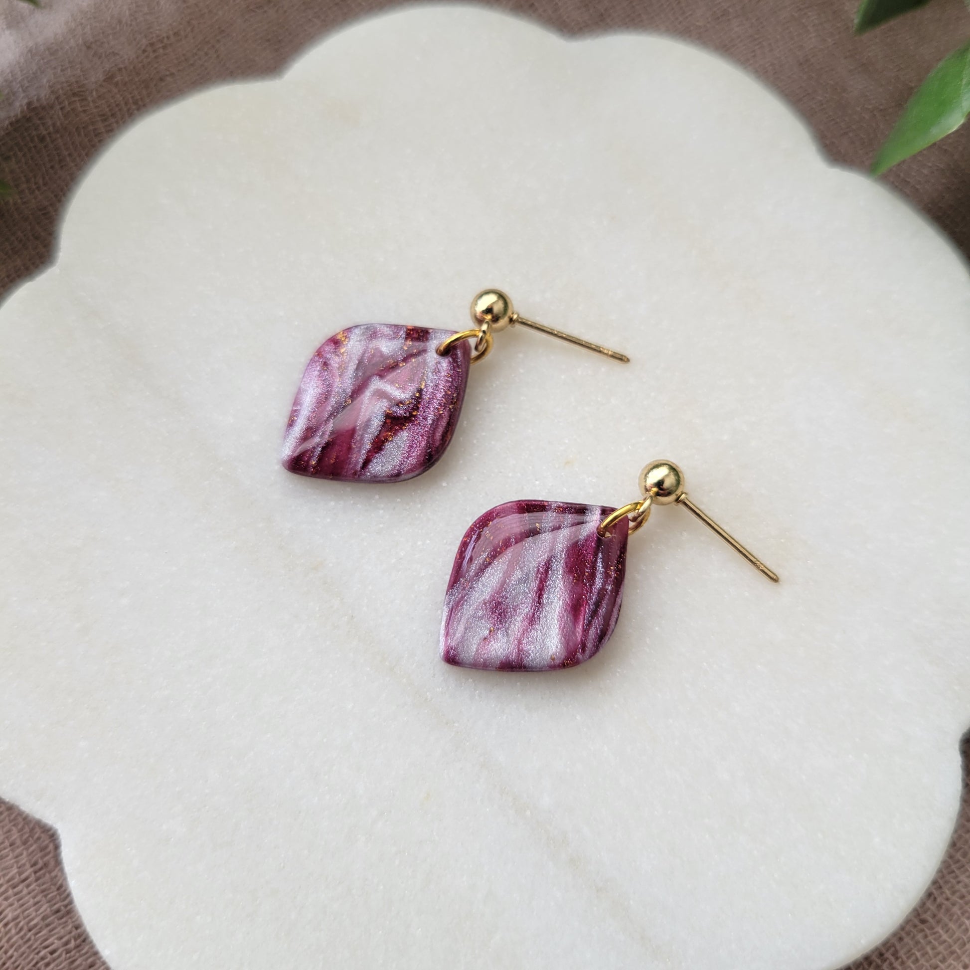 Right side view of a pair of burgundy, pearl marble diamond shaped earrings displayed on a white round scalloped tray.