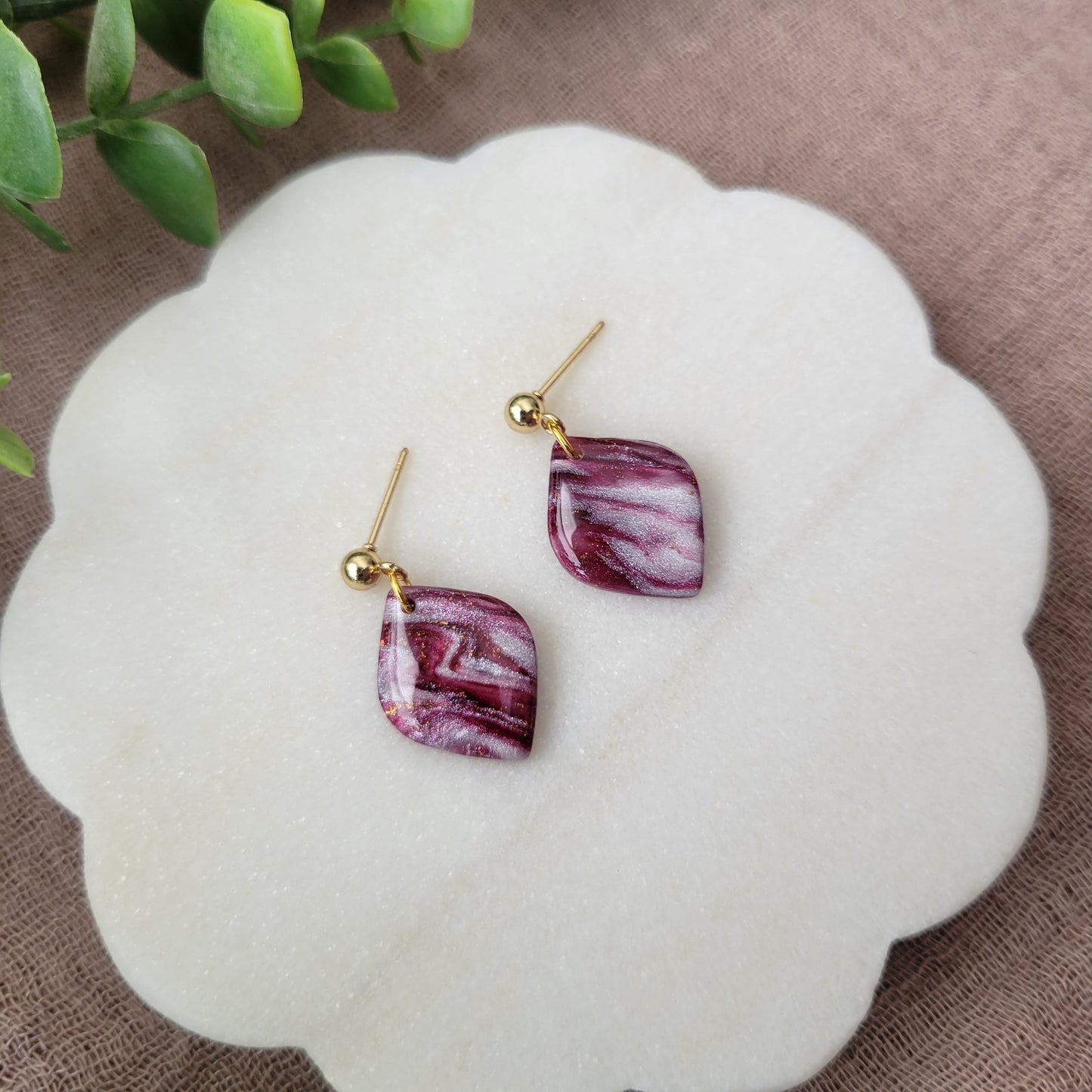 Left side view of a pair of burgundy, pearl marble diamond shaped earrings displayed on a white round scalloped tray.
