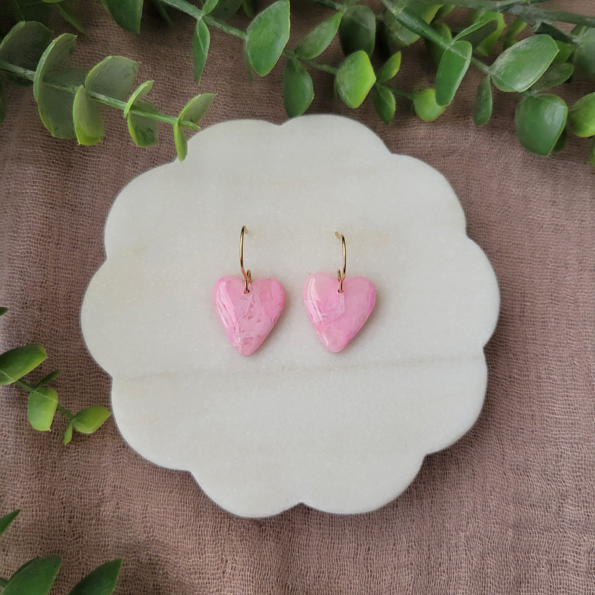 Top view of a pair of pink marble heart earrings displayed on a white round scalloped tray.