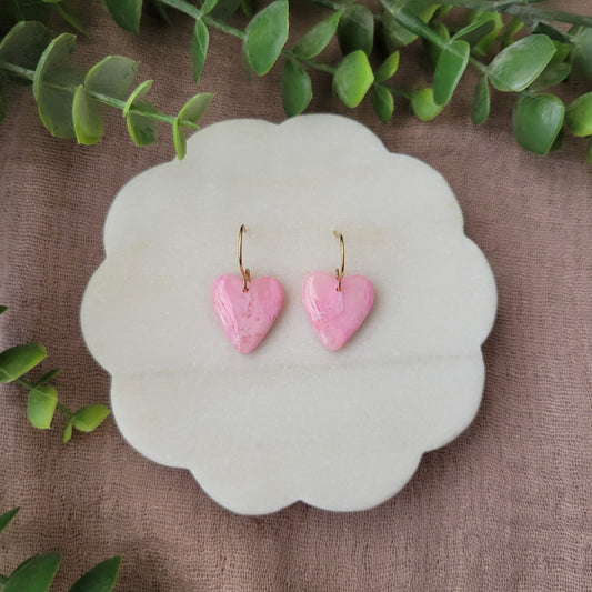 Top view of a pair of pink marble heart earrings displayed on a white round scalloped tray.