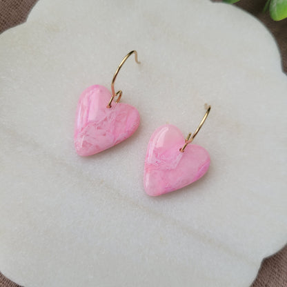 Close up top view of a pair of pink marble heart earrings displayed on a white round scalloped tray.