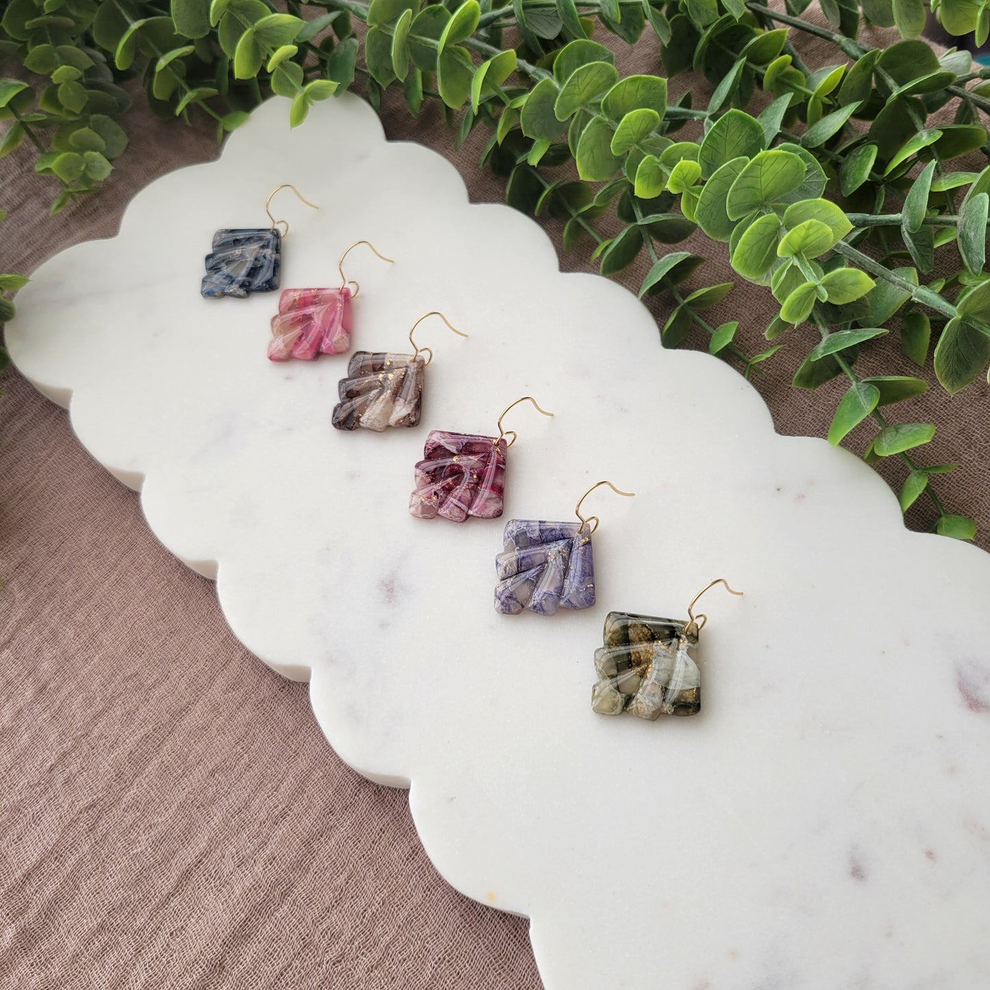 Side view of six marbled earrings displayed on a white scalloped tray.