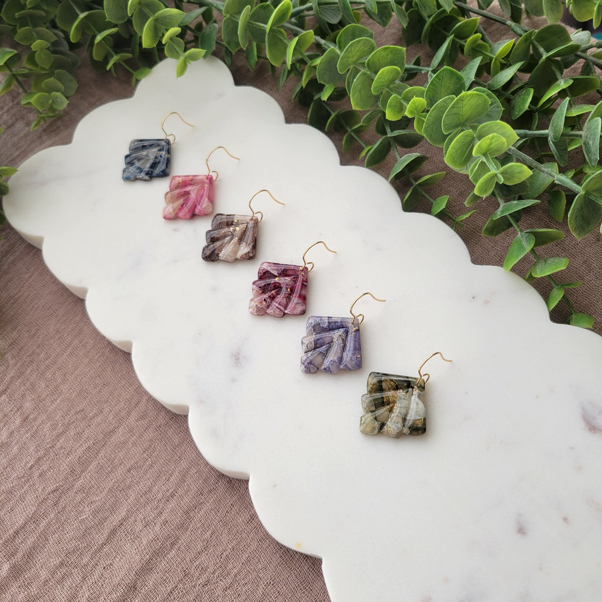 Side view of six marbled earrings displayed on a white scalloped tray.