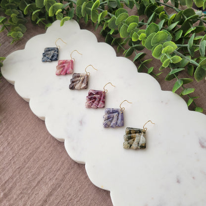 Side view of six marbled earrings displayed on a white scalloped tray.