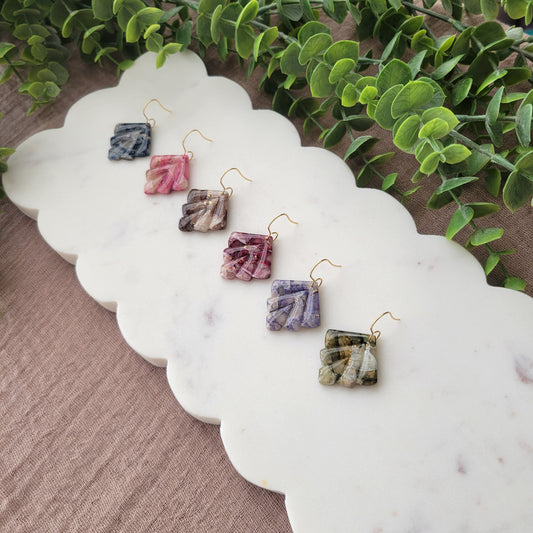 Side view of six marbled earrings displayed on a white scalloped tray.