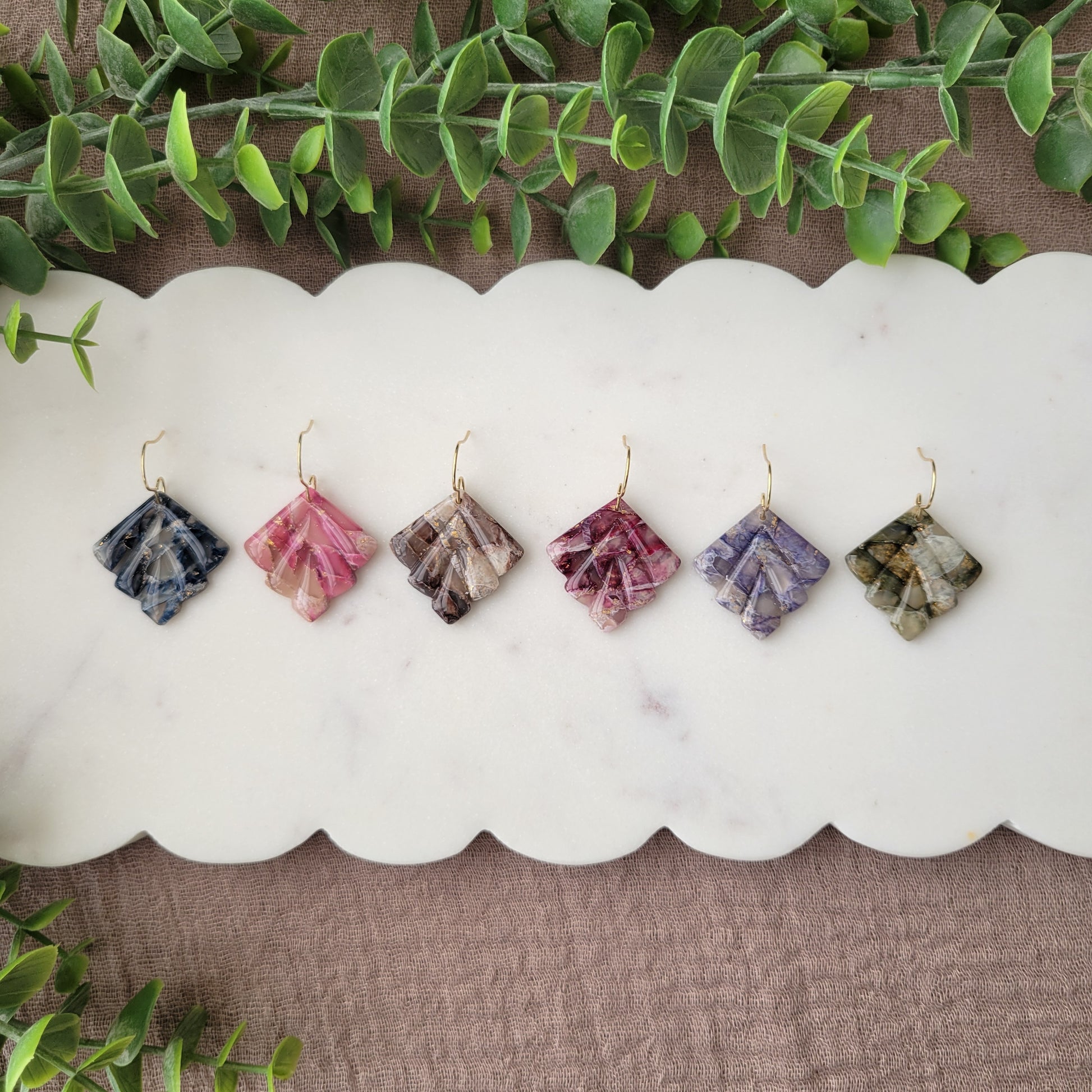 Top view of six marbled earrings displayed on a white scalloped tray.