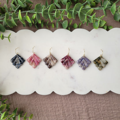 Top view of six marbled earrings displayed on a white scalloped tray.