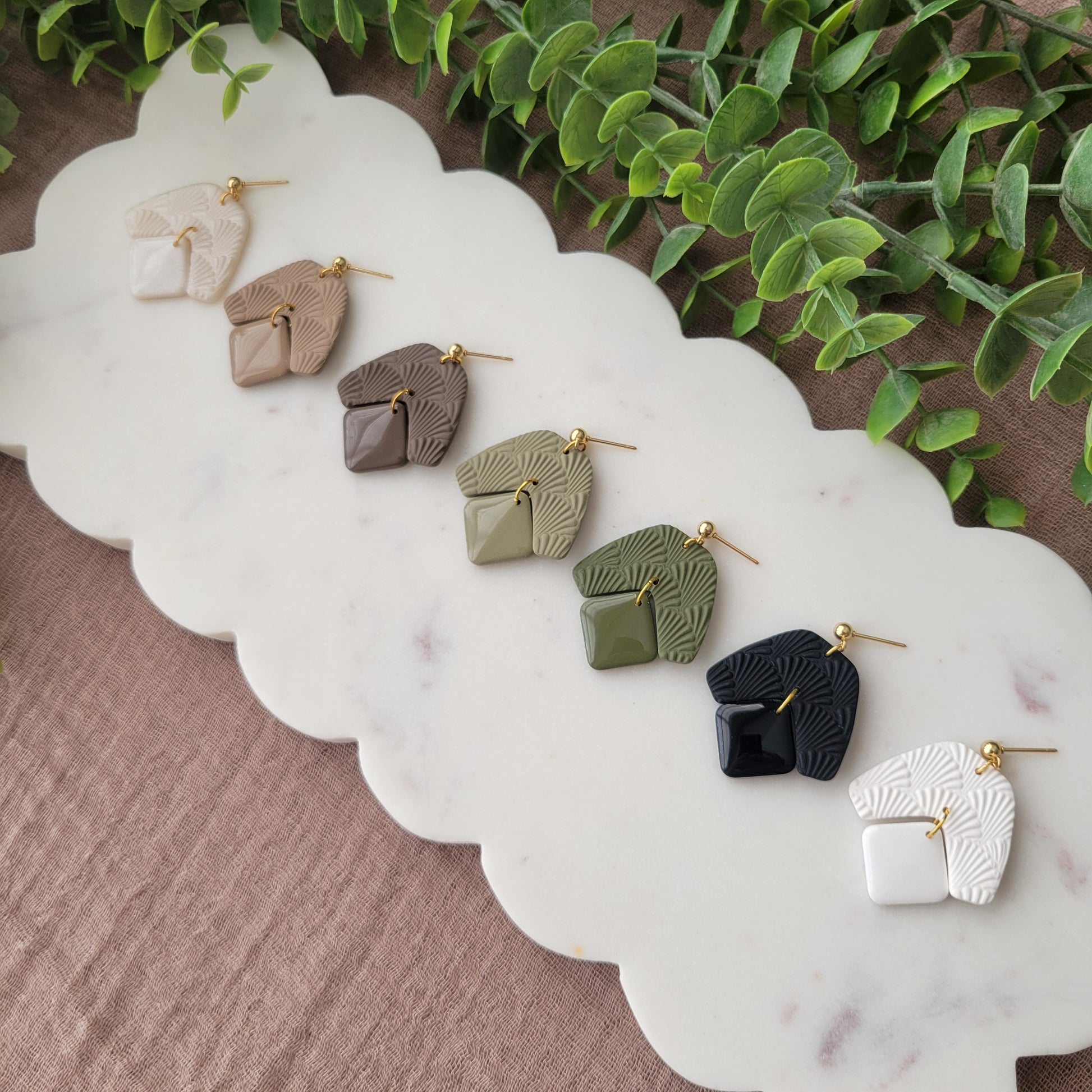 Side view of seven earrings with a scalloped texture displayed on a white scalloped tray.