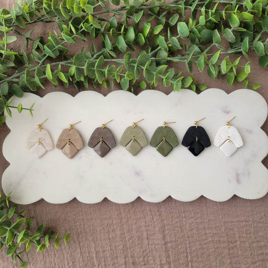 Top view of seven earrings with a scalloped texture displayed on a white scalloped tray.