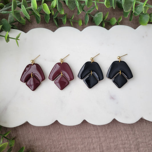 Top view of two pairs of earrings with shiny resin displayed on a white scalloped tray.