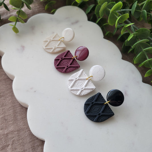 Side view of four earrings with deco diamond texture displayed on a white scalloped tray.