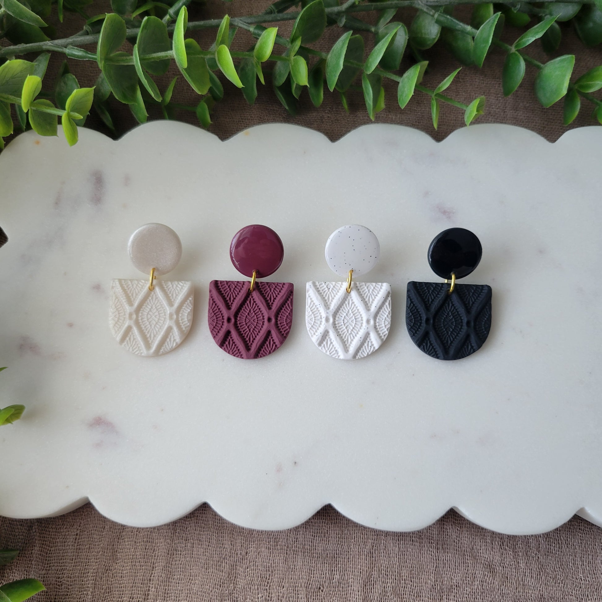 Top view of four earrings with deco diamond texture displayed on a white scalloped tray.