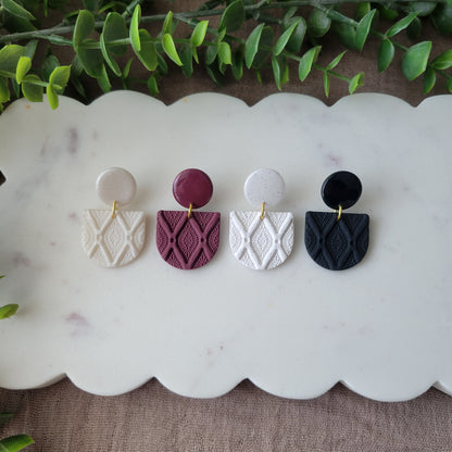 Top view of four earrings with deco diamond texture displayed on a white scalloped tray.